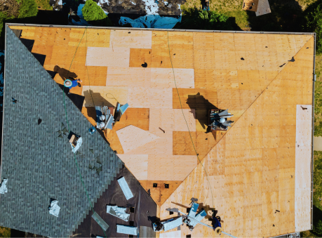 Aerial view of a residential roof replacement in progress, showing workers installing new plywood decking