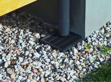 Black downspout connected to a ground-level drainage system surrounded by decorative gravel – downspout installation and drainage.