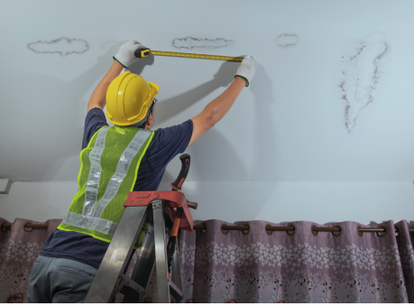 Contractor measuring water stains on a ceiling during a roof leak repair assessment in a residential home