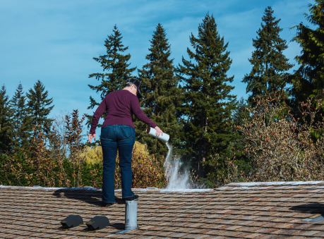 Homeowner performing roof maintenance by applying treatment on shingles to prevent moss and algae growth