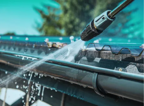Professional gutter cleaning using a high-pressure water hose to remove debris from metal gutters.