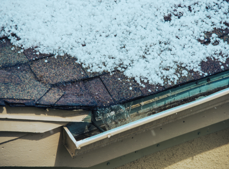 Roof covered in hailstones with overflowing gutter — hail damage roofing contractors protecting homes from storm damage.